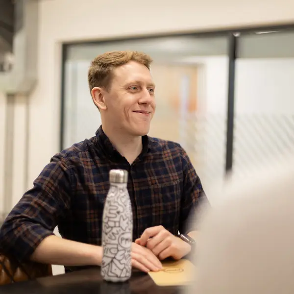 Ben smiling by a standing desk with PMW branded bottle in front of him.