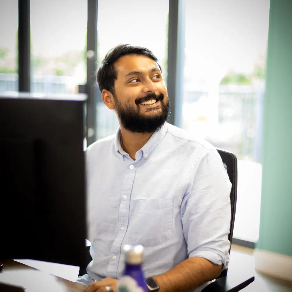 An image of Shashwat sitting at his desk smiling at someone out of shot.