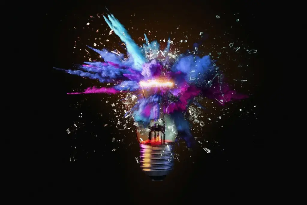 Black background, lit up light bulb exploding with purple, indigo and turquoise smoke.