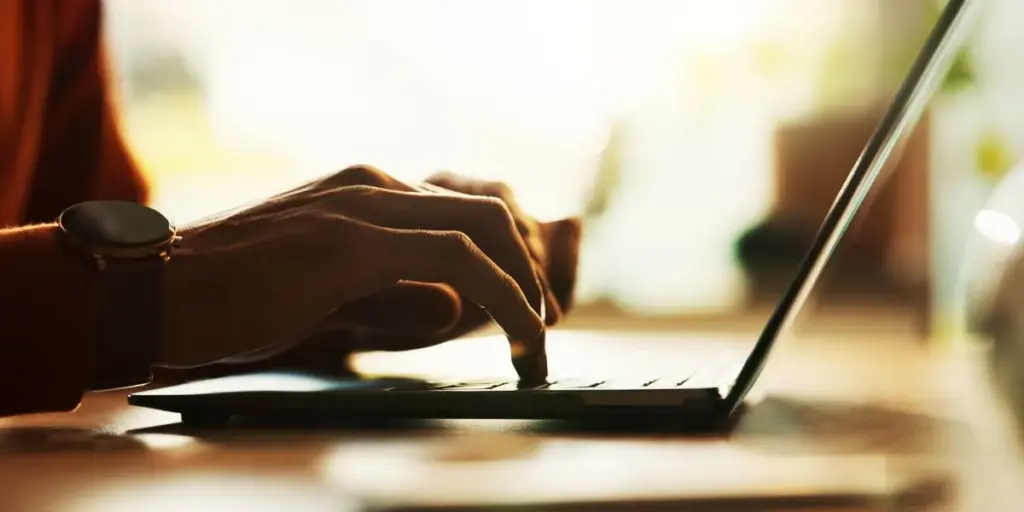 Laptop open on desk with hands typing - in moody lighting.