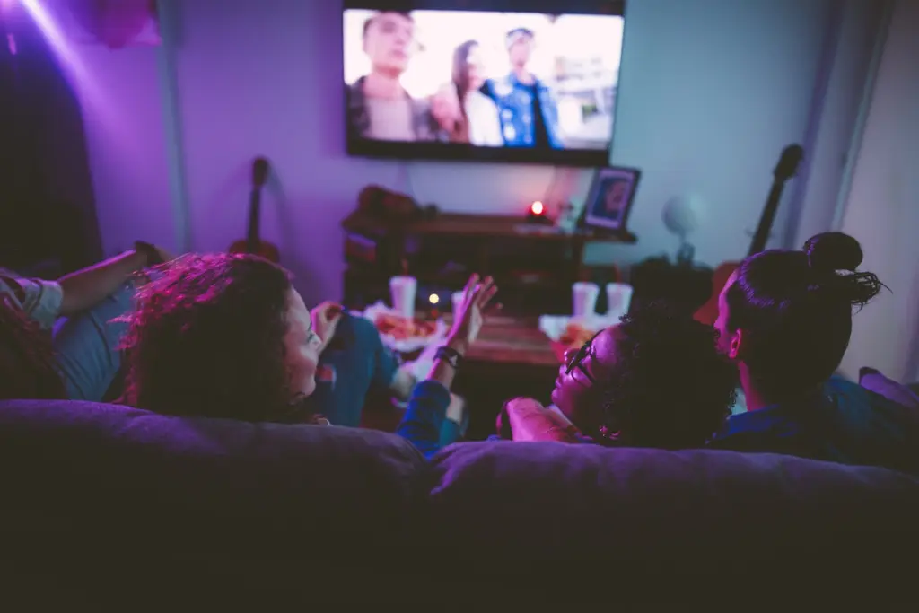 Four people sitting on a sofa in a darkened room watching television.
