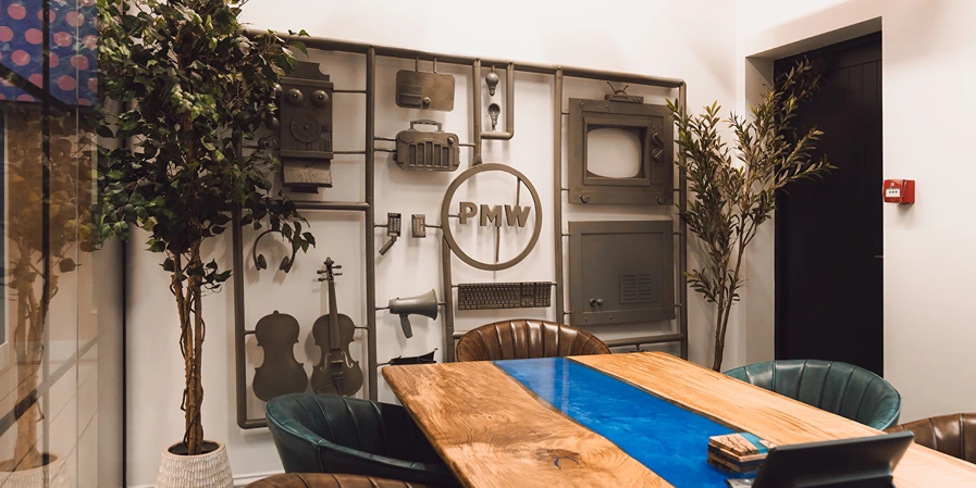 One of the news studios at PMW. Wooden table with blue resin through the middle in front of a piece of artwork showing the PMW logo.