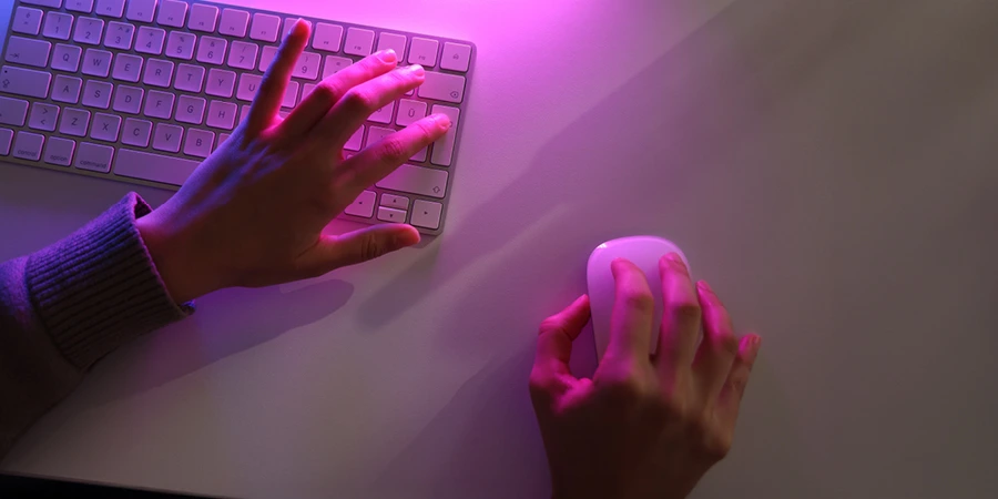 Close up image of a left hand on a computer keyboard and a right hand on a computer mouse.