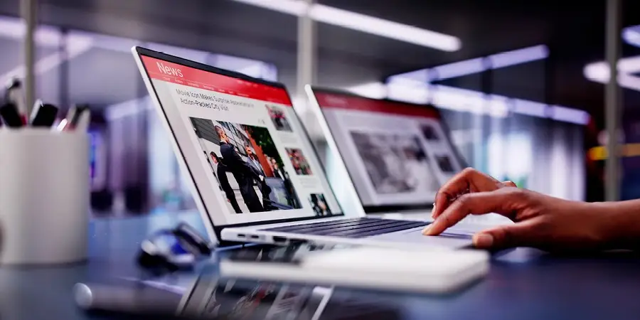 Hand using a mouse pad on a laptop. Screen on laptop is showing a news story.